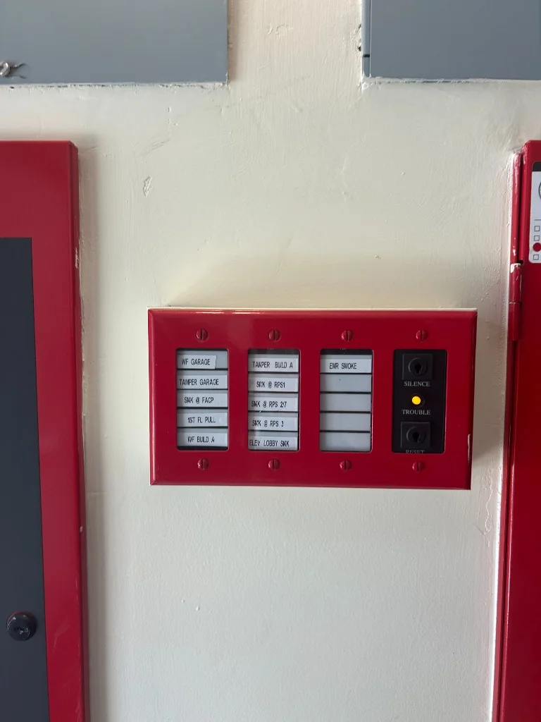Red fire alarm zone annunciator panel displaying trouble and silence indicators