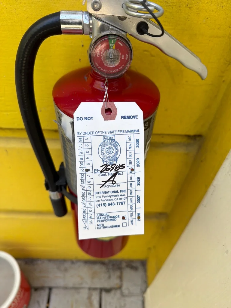 Wall-mounted portable fire extinguisher next to exterior entry door at 1034 Natoma St multi-unit building in Mission District, San Francisco.