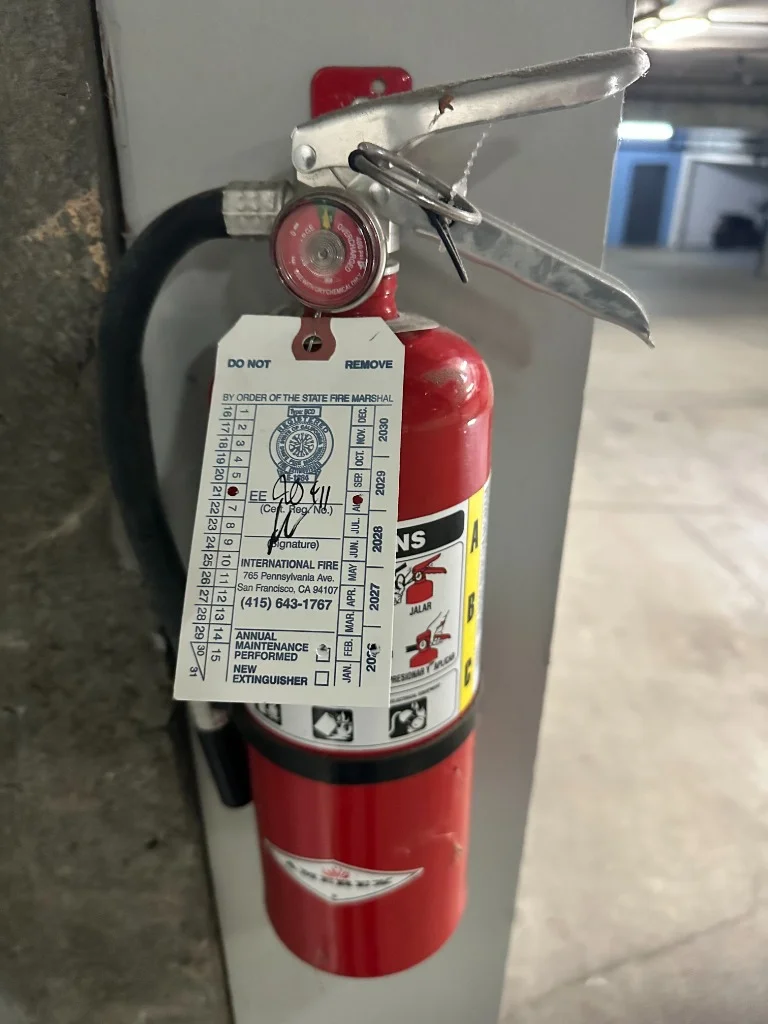 Wall-mounted Amerex fire extinguisher with official California Title 19 certification tag on grey concrete wall at Castro District, San Francisco, CA by International Fire Inc.
